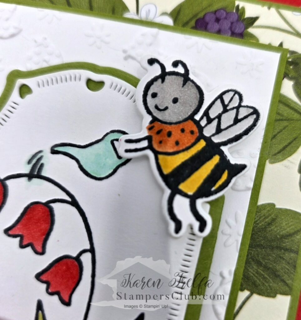 Close-up detail of a hand-colored bee with a watering can from the Sweet Bugs Stampin' Up stamp set on a white embossed card panel with red bell flowers