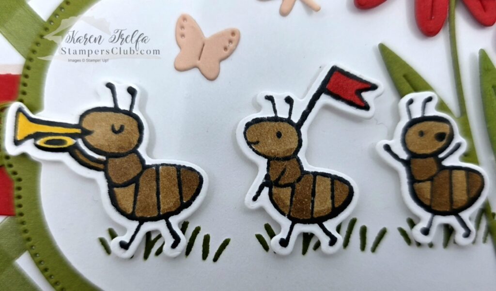 Close-up of three hand-colored marching ants from the Sweet Bugs Stampin' Up stamp set, one with a yellow trumpet and one with a red flag, with small butterfly die cuts in the background